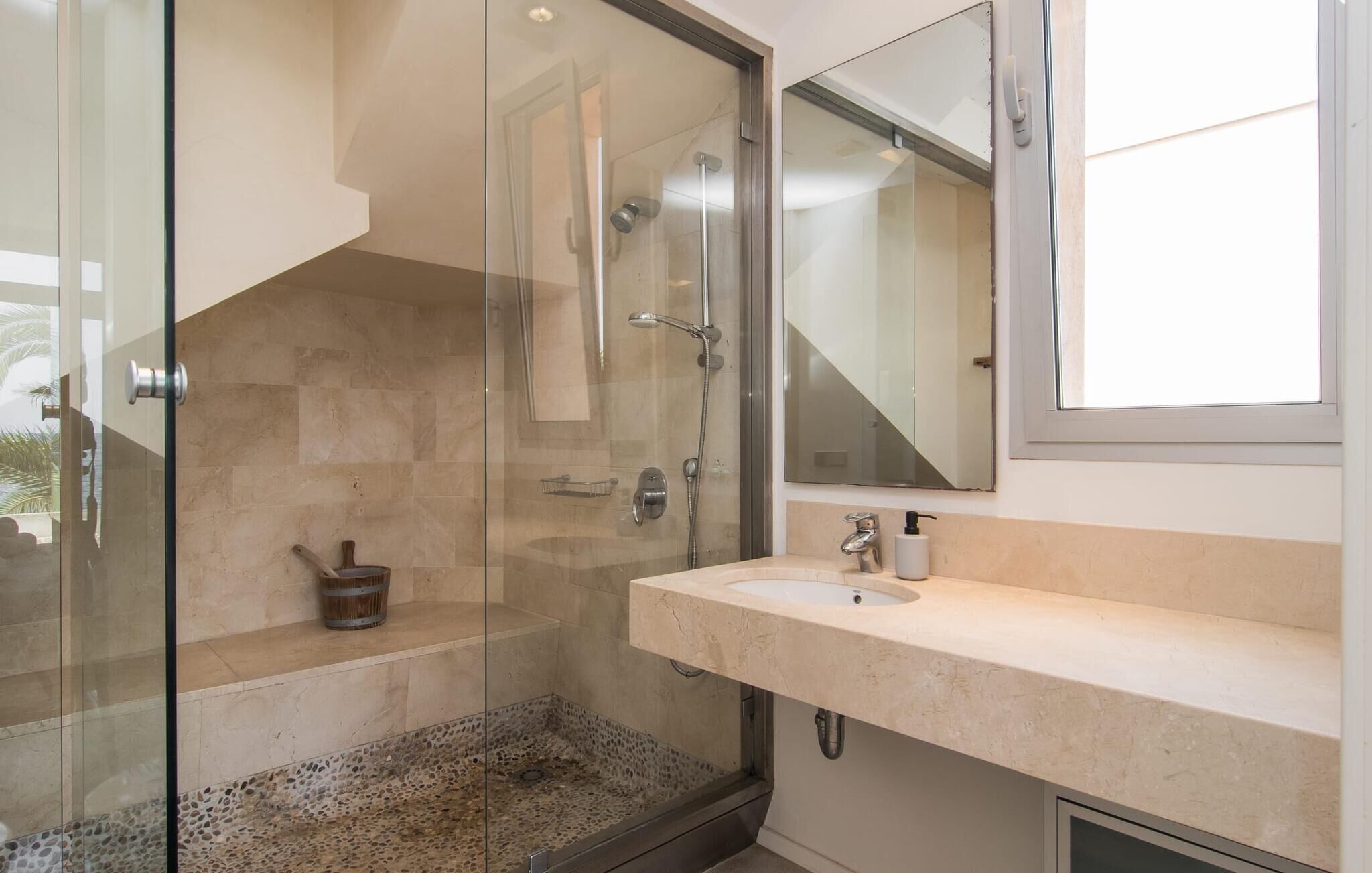 A modern bathroom with a glass-enclosed shower, a beige marble sink, and a large mirror.