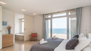 Een slaapkamer met een groot bed, een stoel, een bureau en uitzicht op het strand.