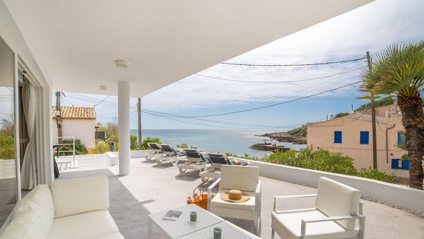 A balcony with white furniture, a view of the sea, and a building with blue windows. - Amazing home in Cala Ratjada with WiFi (Cala Ratjada)