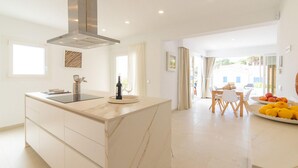 A modern kitchen with a central island, a dining area with a table and chairs, and a view of the outdoors. - Amazing home in Cala Ratjada with WiFi (Cala Ratjada)