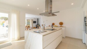 A modern kitchen with a marble island, stainless steel range hood, and a dining area with a TV. - Amazing home in Cala Ratjada with WiFi (Cala Ratjada)