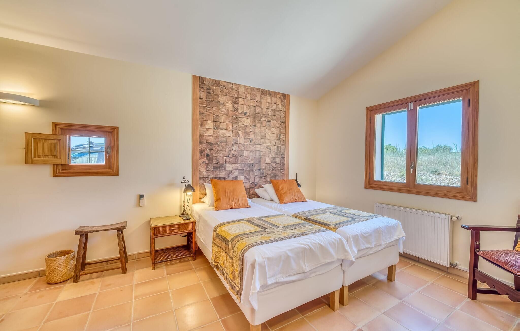 A bedroom with a large bed, a wooden headboard, a nightstand, a lamp, a chair, and a window with a view of the outdoors.
