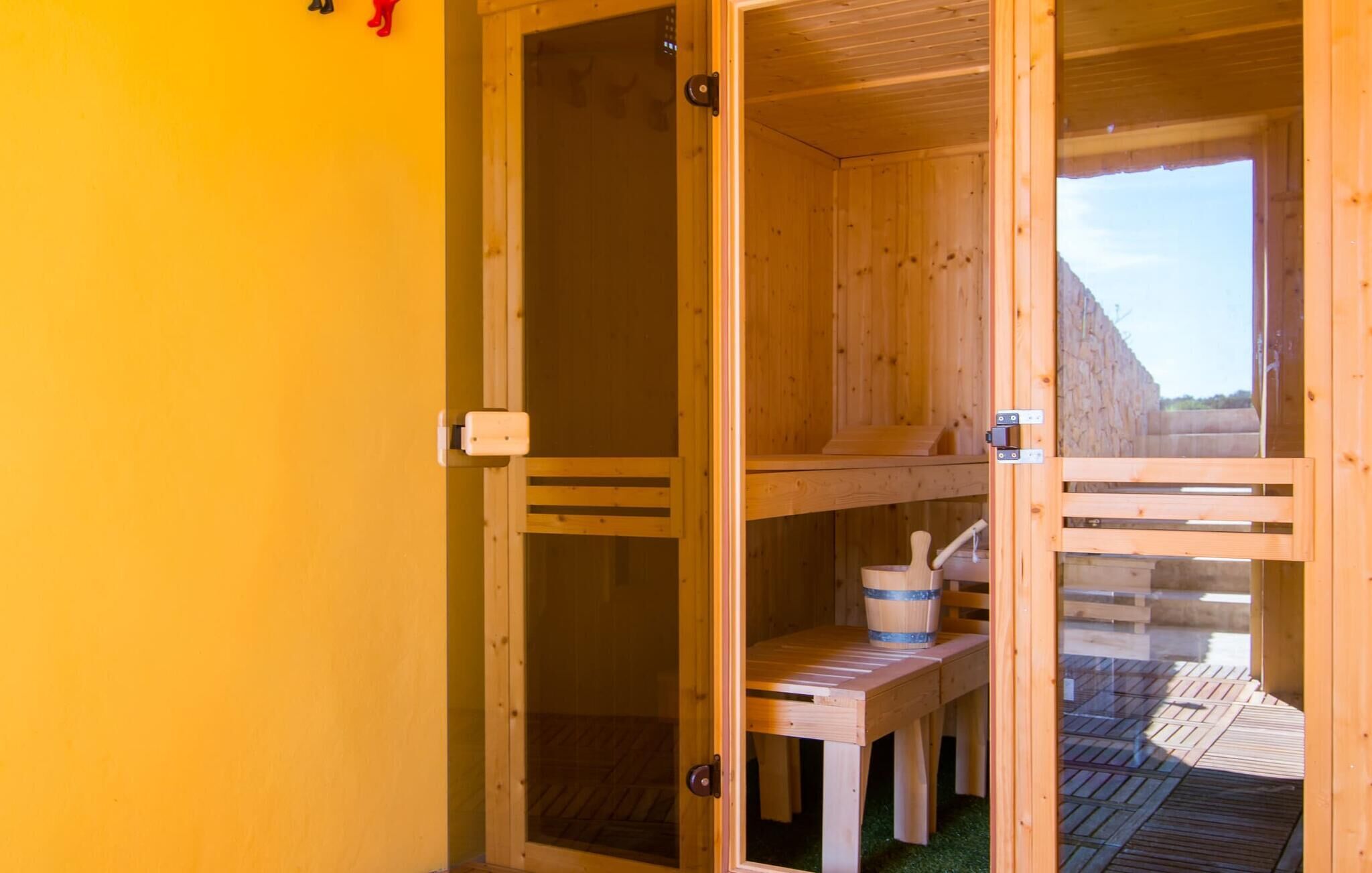 A wooden sauna with a bench and a bucket, a glass door, and a view of a wooden deck outside.