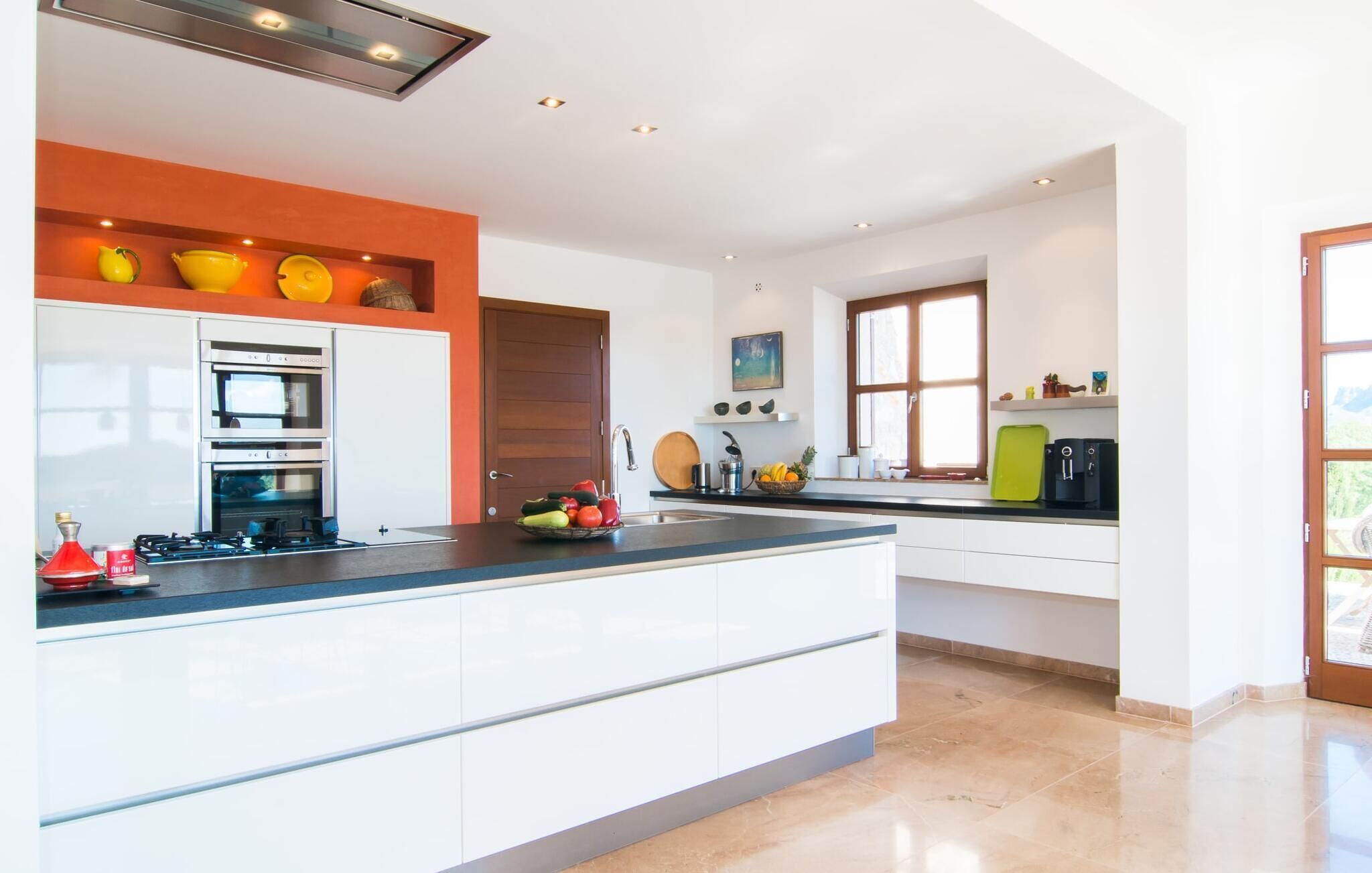 Een moderne keuken met een centraal eiland, een inbouwoven en een raam dat natuurlijk licht binnenlaat.