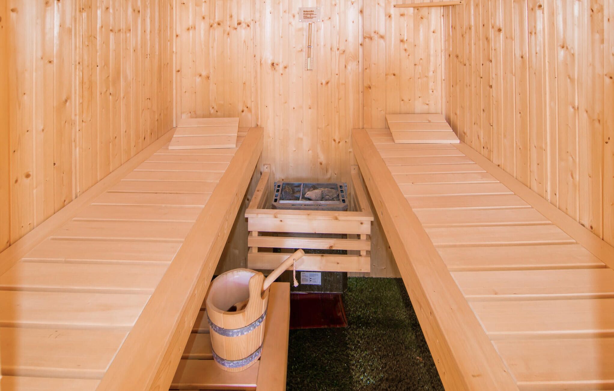 A sauna room with wooden benches and a central stone heating element.