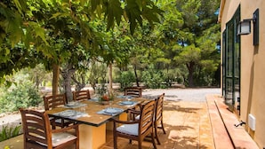 Un espace de restauration en plein air avec une table dressée pour quatre personnes, entouré d’arbres et d’un bâtiment doté de grandes fenêtres.