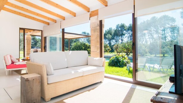 A modern living room with a white sofa, wooden beams, large windows, and a view of greenery. - Cozy home in Port Verd with private swimming pool, can be inside or outside (Port Verd)
