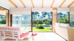A bright room with a white sofa, a pink and white striped bench, and a view of a garden through large windows. - Cozy home in Port Verd with private swimming pool, can be inside or outside (Port Verd)