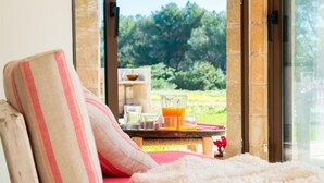 A cozy seating area with a view of a lush garden, a tray with a glass of orange juice, and a red cushion. - Cozy home in Port Verd with private swimming pool, can be inside or outside (Port Verd)