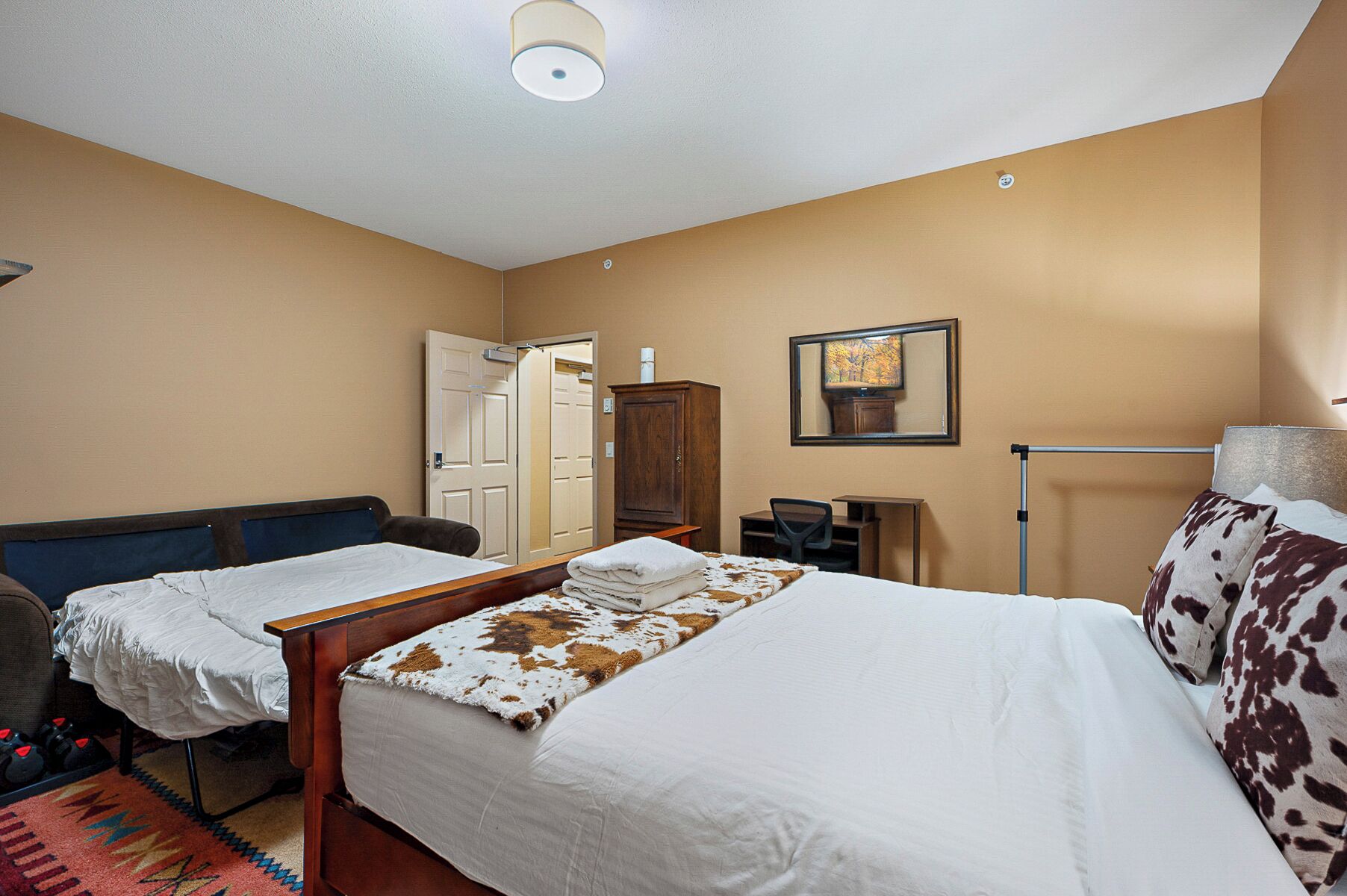 Hotellihuone, jossa on kaksi sänkyä, vaatekaappi, työpöytä, tuoli ja peili.
