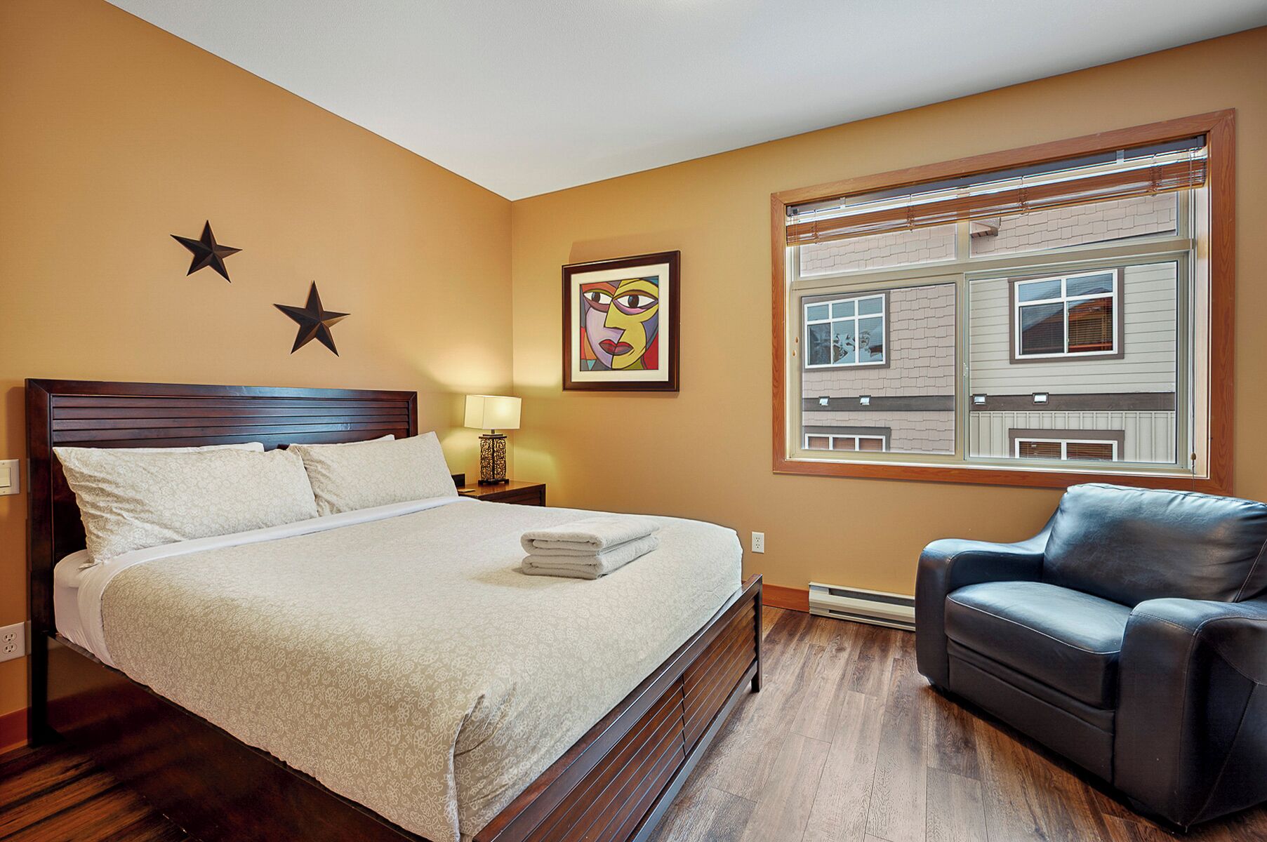 Une chambre d’hôtel avec un lit, une table de chevet, une lampe, une chaise, une décoration en forme d’étoile et une fenêtre donnant sur des immeubles.