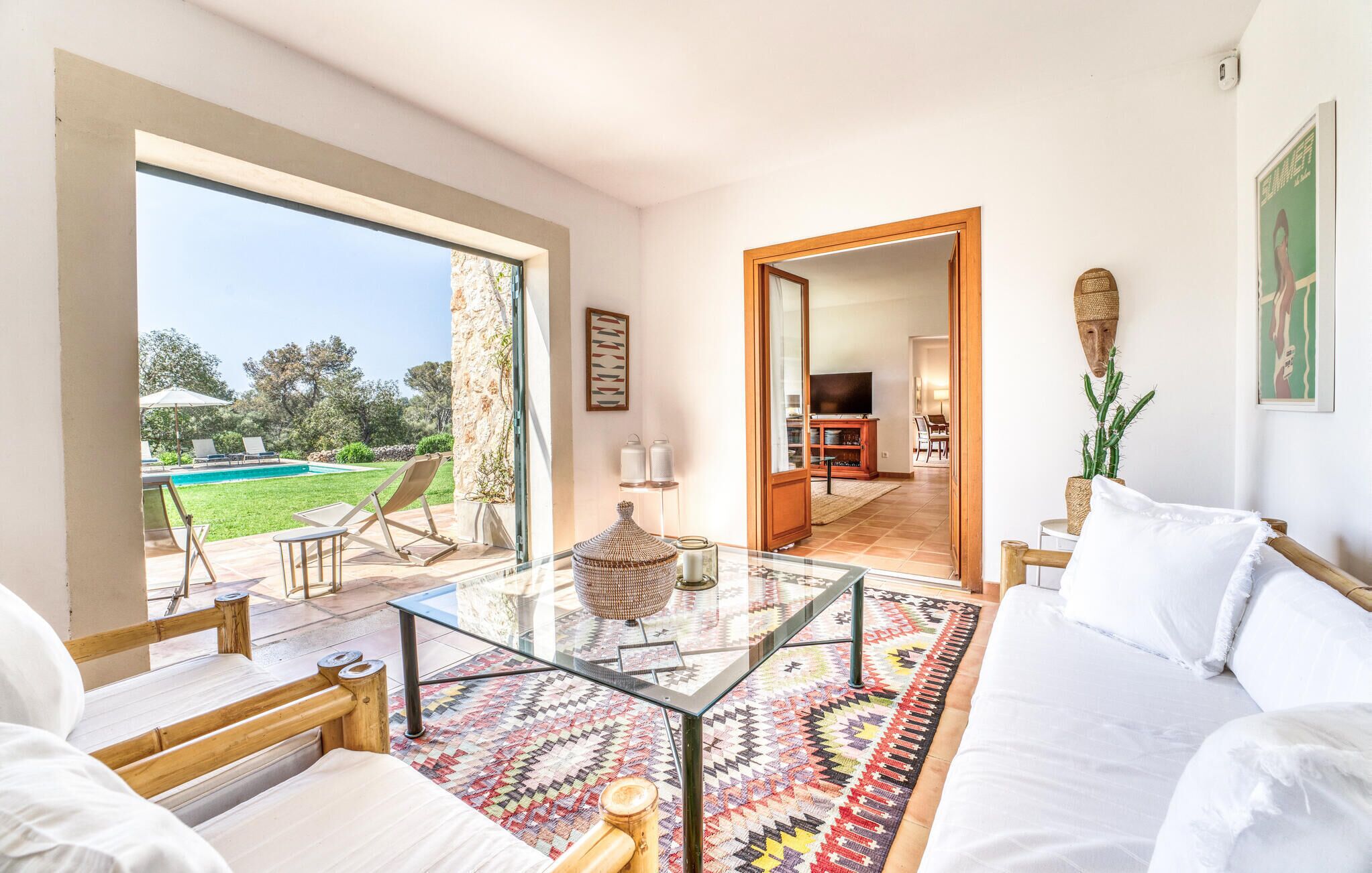A spacious living area with a glass coffee table, a patterned rug, and a view of a pool and garden.