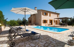 Un área junto a la piscina con sillones de descanso, sombrillas y un patio de piedra.