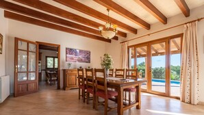 A spacious dining area with wooden furniture, a chandelier, and a large window offering a view of a swimming pool. - Awesome home in Alqueria Blanca (Alqueria Blanca)