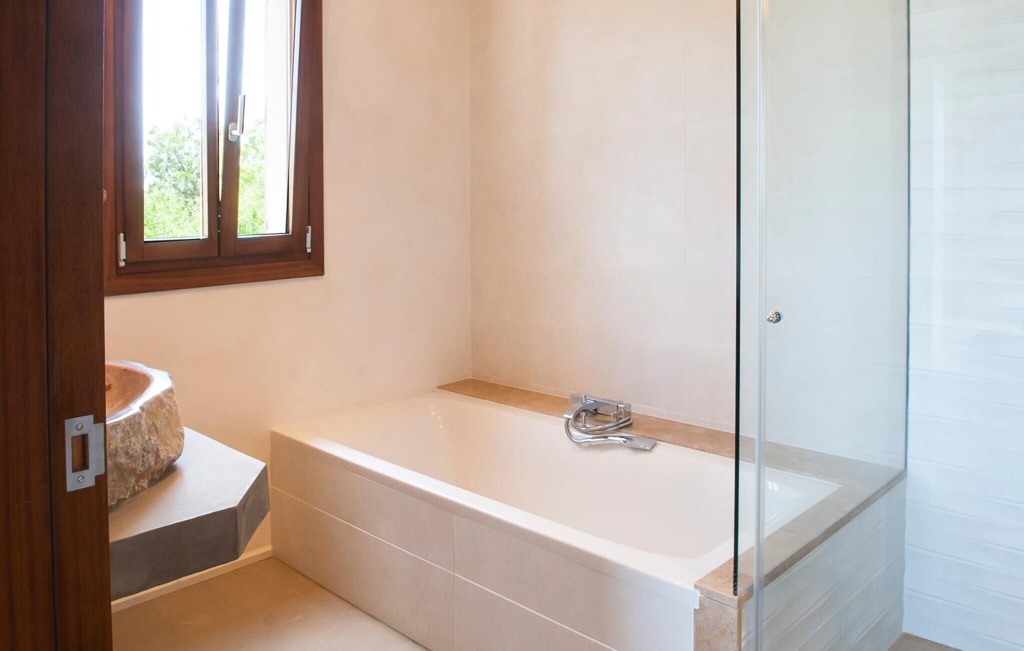 Un bany modern amb banyera, un espai de dutxa amb envàs de vidre i una finestra que deixa entrar llum natural.