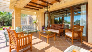 Un patio con mobiliario de madera, una mesa de vidrio y vistas al exterior.
