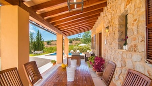 Une terrasse extérieure aménagée avec du mobilier en bois, un mur en pierre et une vue sur une piscine et la verdure.