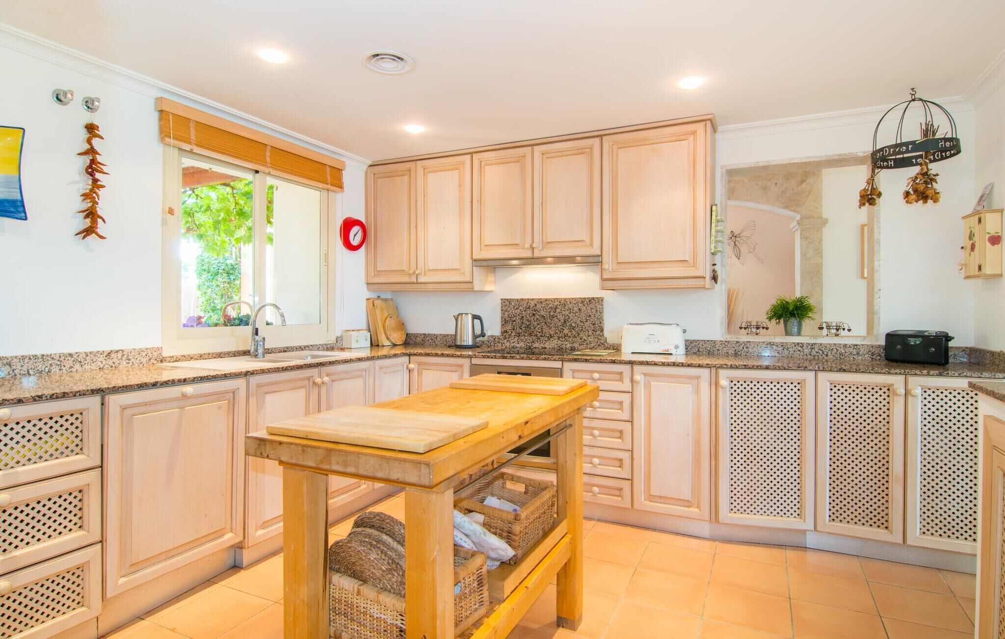 A kitchen with wooden cabinets, a granite countertop, a wooden table, and a window with a view of greenery.