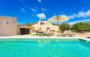 Une villa en pierre dotée d’une piscine, d’un espace salon extérieur et d’un grand parasol.