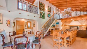 A spacious dining area with a high ceiling and wooden beams, a staircase leading to an upper level, and a stone wall in the background. - Pet friendly home in Can Picafort (Can Picafort)