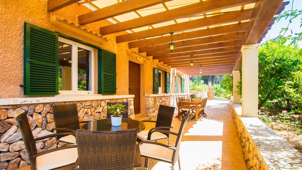 Eine Terrasse im Freien mit Korbmöbeln, Steinmauern und grünen Fensterläden.