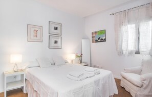 Habitación de hotel con cama, una silla, mesita de noche, espejo y obras de arte en las paredes.
