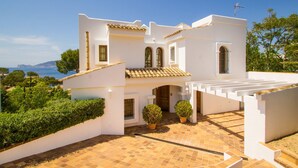 Una villa blanca con un patio con tejas, vista al mar y una pérgola.
