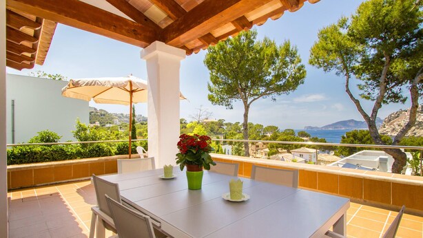 Un patio al aire libre con una mesa y sillas, una planta en maceta y vistas al mar y a las colinas.