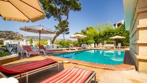 Zona de piscina con sillas de descanso, sombrillas y vistas del paisaje circundante.