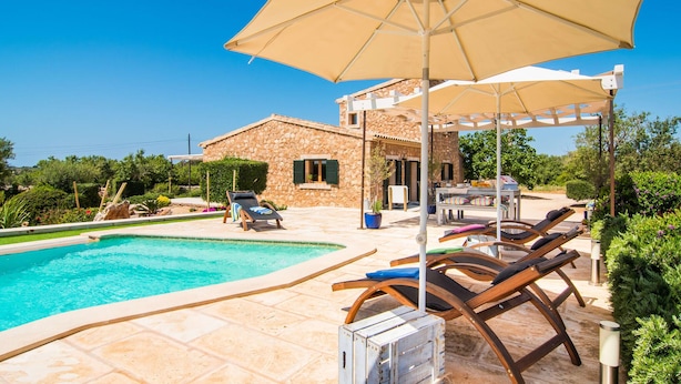 Un espace piscine avec des chaises longues et des parasols, un bâtiment en pierre et une vue sur la mer.