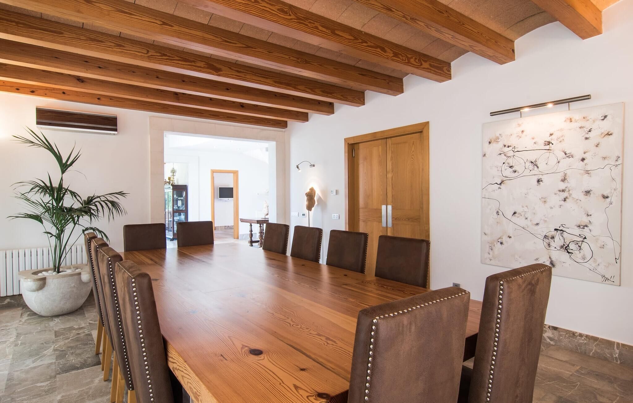 Un comedor con una mesa y sillas de madera, una planta en maceta y una obra de arte colgada en la pared.
