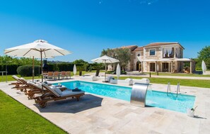A swimming pool with lounge chairs and umbrellas, a stone house with a garden, and a clear blue sky. - Cozy home in Selva with private swimming pool, can be inside or outside (Selva)