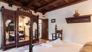 Ein Hotelzimmer mit großem Holzschrank, einem Bett mit weißer Bettwäsche, einem Sessel und einem kleinen Tisch.