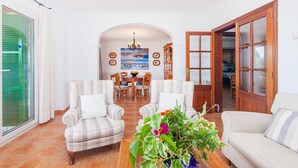 Ein geräumiges Wohnzimmer mit Essbereich, ausgestattet mit gestreiften Sesseln, einem Sofa, einem Couchtisch mit Blumen und Blick durch einen offenen Durchgang zur Küche.