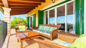 Eine Terrasse im Freien mit Korbmöbeln, einem Holztisch und einem überdachten Bereich mit Holzbalken.