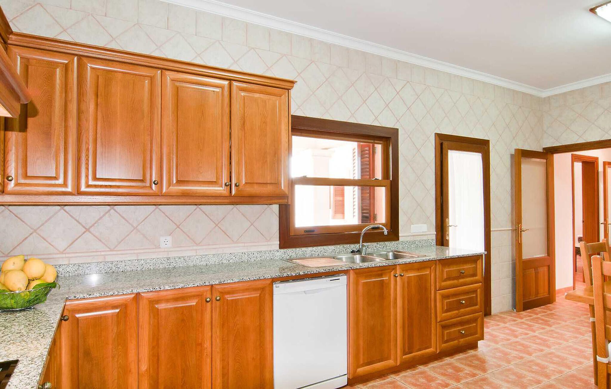 A kitchen with wooden cabinets, a granite countertop, a built-in dishwasher, and a window with blinds.