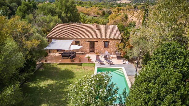 Uma casa de pedra com telhado em tijolos, piscina e área de estar externa.