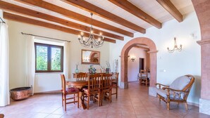 A spacious dining area with wooden furniture, a chandelier, and a view of greenery outside. - Beautiful home in Cala Murada (Cala Murada)