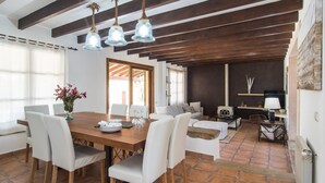 Een ruime eethoek met een houten tafel en witte stoelen, een houten plafond met zichtbare balken, en een gezellige zithoek met een bank en fauteuils.