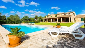 Ein Pool mit Liegestühlen, eine Steinterrasse und ein großes Haus mit Garten.