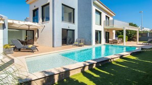 Ett modernt hus i två våningar med en swimmingpool, utomhusmöbler och en täckt uteplats.