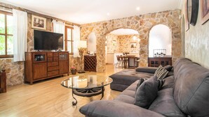 A spacious living room with a stone wall, a television, a glass coffee table, and a sofa. - Lovely home in Buger with private swimming pool, can be inside or outside (Buger)