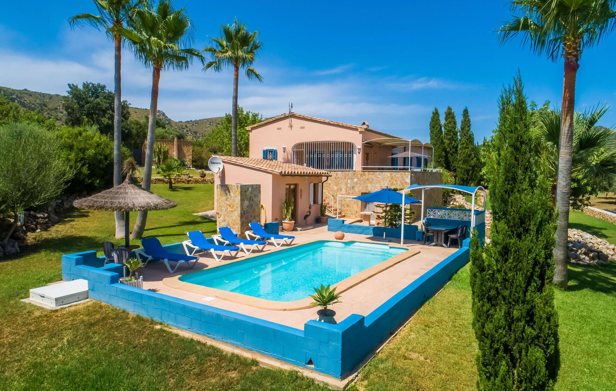 Ein zweistöckiges Haus mit Swimmingpool, blauen Liegestühlen und Palmen.