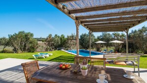 Un’area esterna coperta con piscina, sedie a sdraio e un tavolo con frutta e bicchieri.