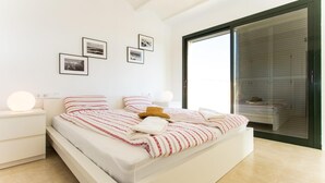 Una camera da letto moderna con un letto grande, pareti bianche e una porta scorrevole in vetro che dà su un balcone.