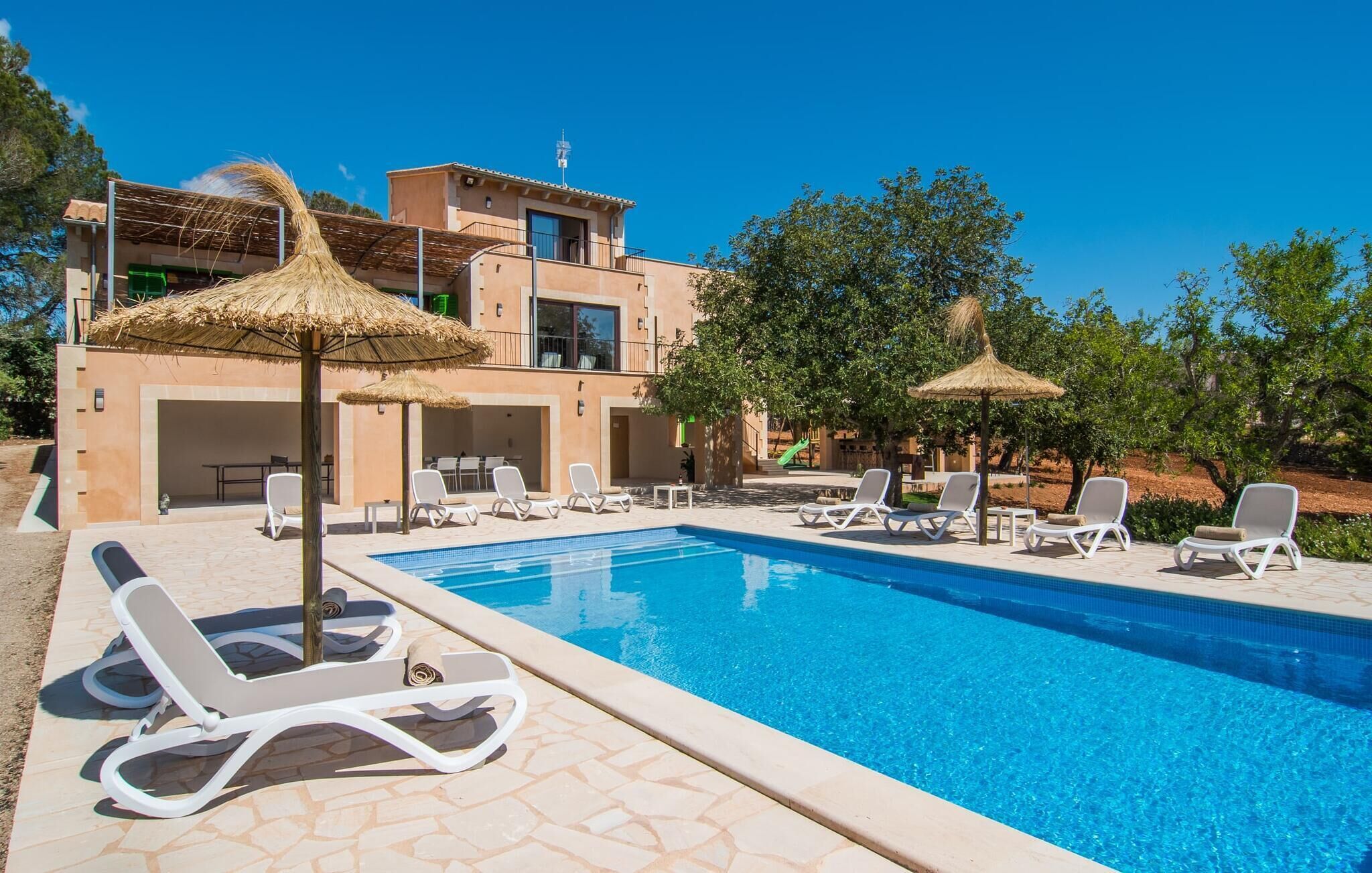 Ein Pool mit Liegestühlen und strohgedeckten Sonnenschirmen, umgeben von einem Gebäude mit Balkon und Rutsche.