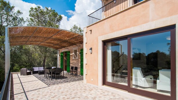 Eine moderne Außenpatio mit einer Pergola, Gartenmöbeln und einer Glastür, die auf einen Balkon führt.