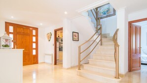 Un pasillo amplio con suelo de mármol, una escalera con barandilla dorada y puertas de madera.
