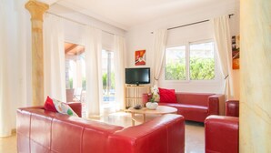 Una sala de estar con sofás de cuero rojo, un televisor de pantalla plana y ventanas grandes con cortinas.