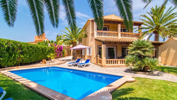 Una casa de dos pisos con piscina, un porche cubierto y un jardín con palmeras.